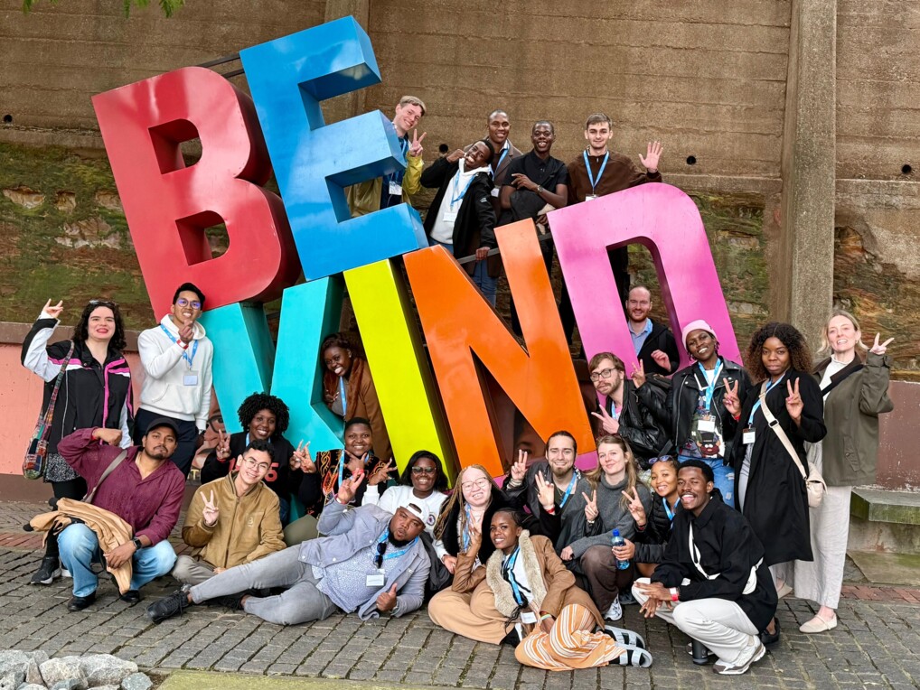 Deltagerne på dette års Peace Messenger Training, poserer foran en "BE KIND" skulptur
