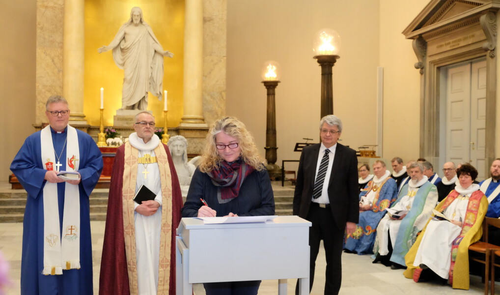 Aftalen bliver underskrevet med en masse vidner. Skulptur af Jesus i baggrunden.
